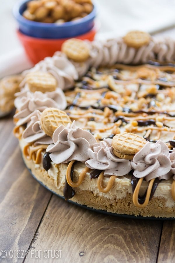 No-Bake Frozen Peanut Butter Cheesecake on a brown board with nuts in a blue bowl in the background 