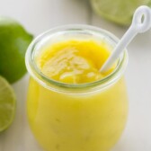 Homemade Lime Curd in In a small clear glass with limes all around the glass