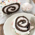 chocolate cake roll filled with ice cream and topped with whipped cream and sprinkles, slice on plate