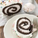 chocolate cake roll filled with ice cream and topped with whipped cream and sprinkles, slice on plate