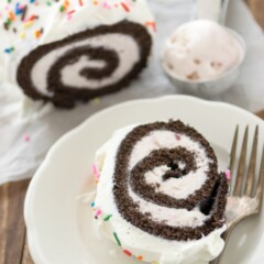 chocolate cake roll filled with ice cream and topped with whipped cream and sprinkles, slice on plate