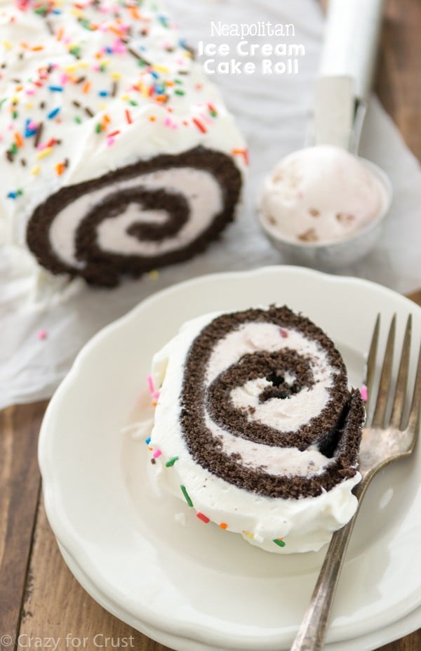 ice cream cake roll with chocolate cake and strawberry ice cream and whipped topping with sprinkles on white plate with fork