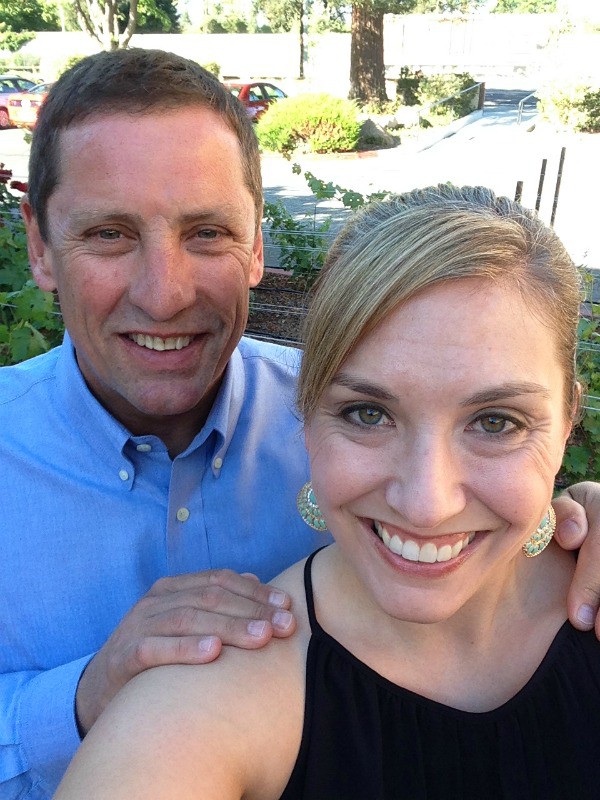 man in blue button down shirt touching the shoulders of a woman with black shirt and teal earrings 