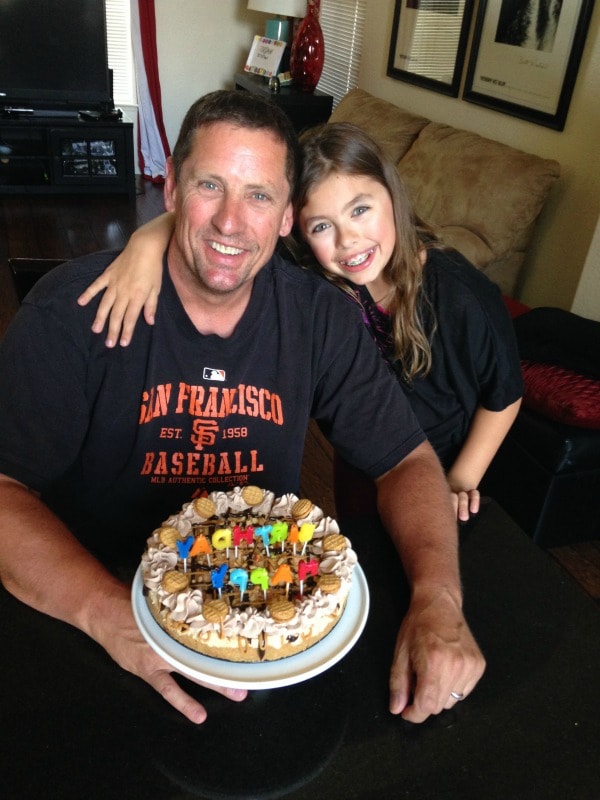 man in a black and orange shirt holding a birthday cake with daughter hugging him