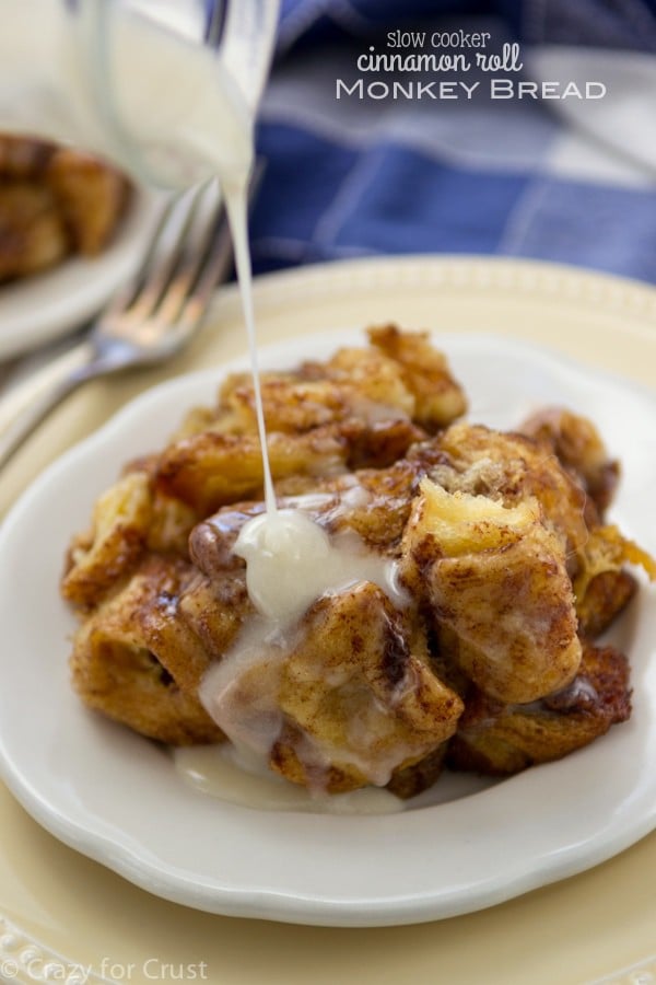 Slow Cooker Cinnamon Roll Monkey Bread on a white plate with a fork and icing being pour over them