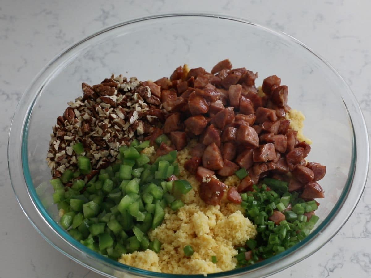 crumbled cornbread with sausage, pecans, green peppers, and green onions in large glass bowl.