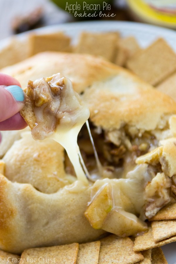 Apple pecan pie baked brie with a woman's hand scooping a cracker, with title.