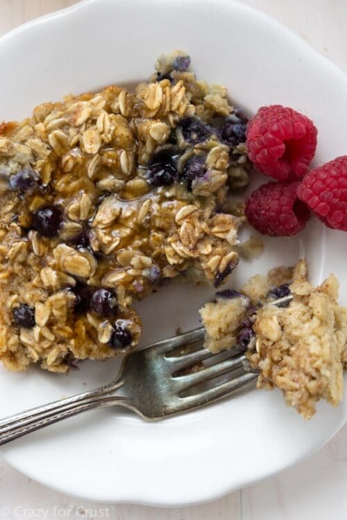 Baked oatmeal on a white plate with a fork and raspberries