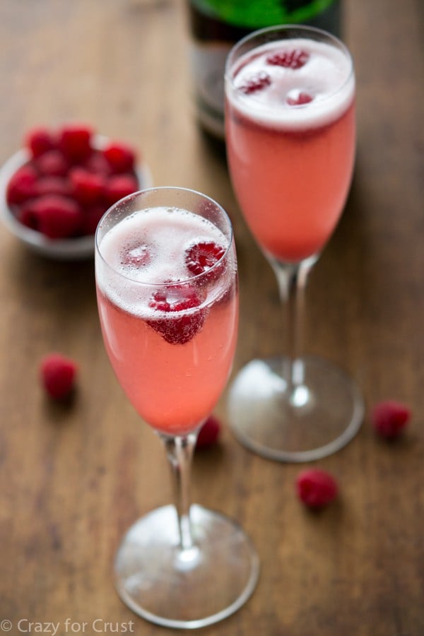 Two Champagne Brunch Bellini Mimosas garnished with fresh raspberries. 