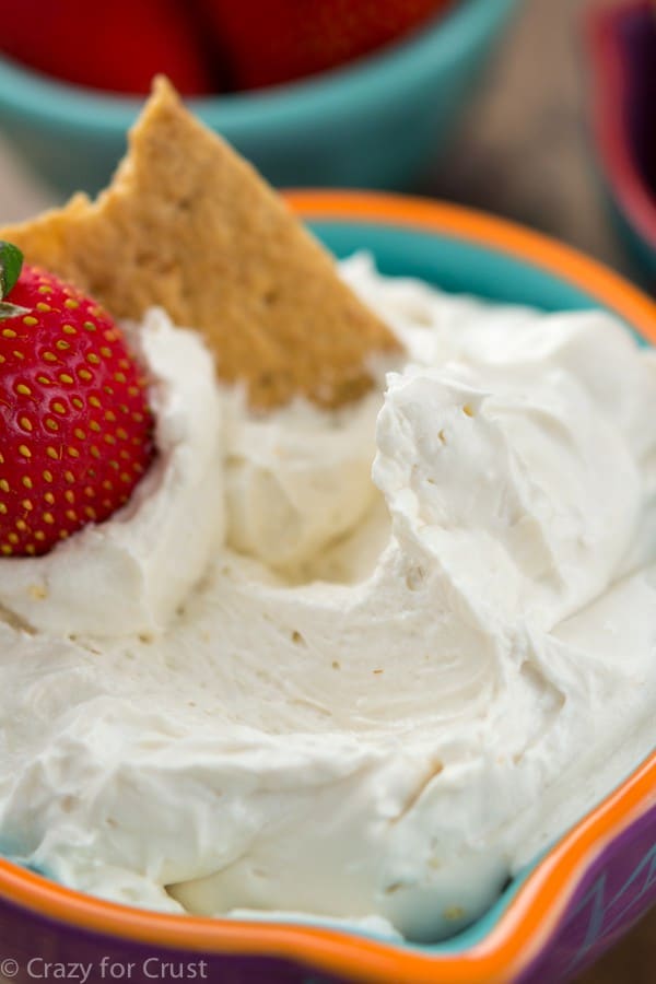 Skinny cheesecake dip in a orange and blue bowl with a graham cracker and a strawberry