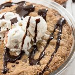 Close up shot of chocolate pecan oatmeal cookie pie with ice cream and chocolate sauce on top