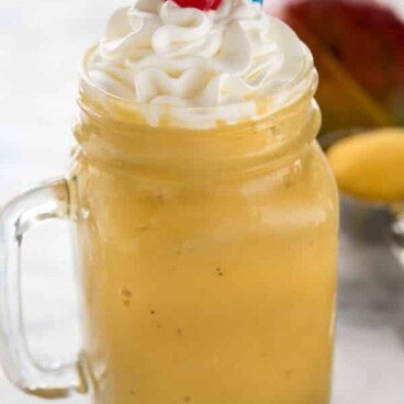 Mango julius drink with whipped cream and cherry on top with blue polka dot straw