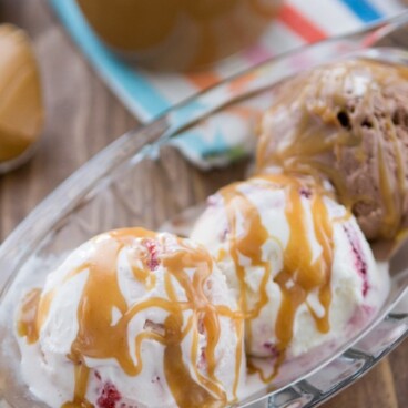 Clear ice cream dish with three scoops of ice cream covered in peanut butter sauce with jar in the background