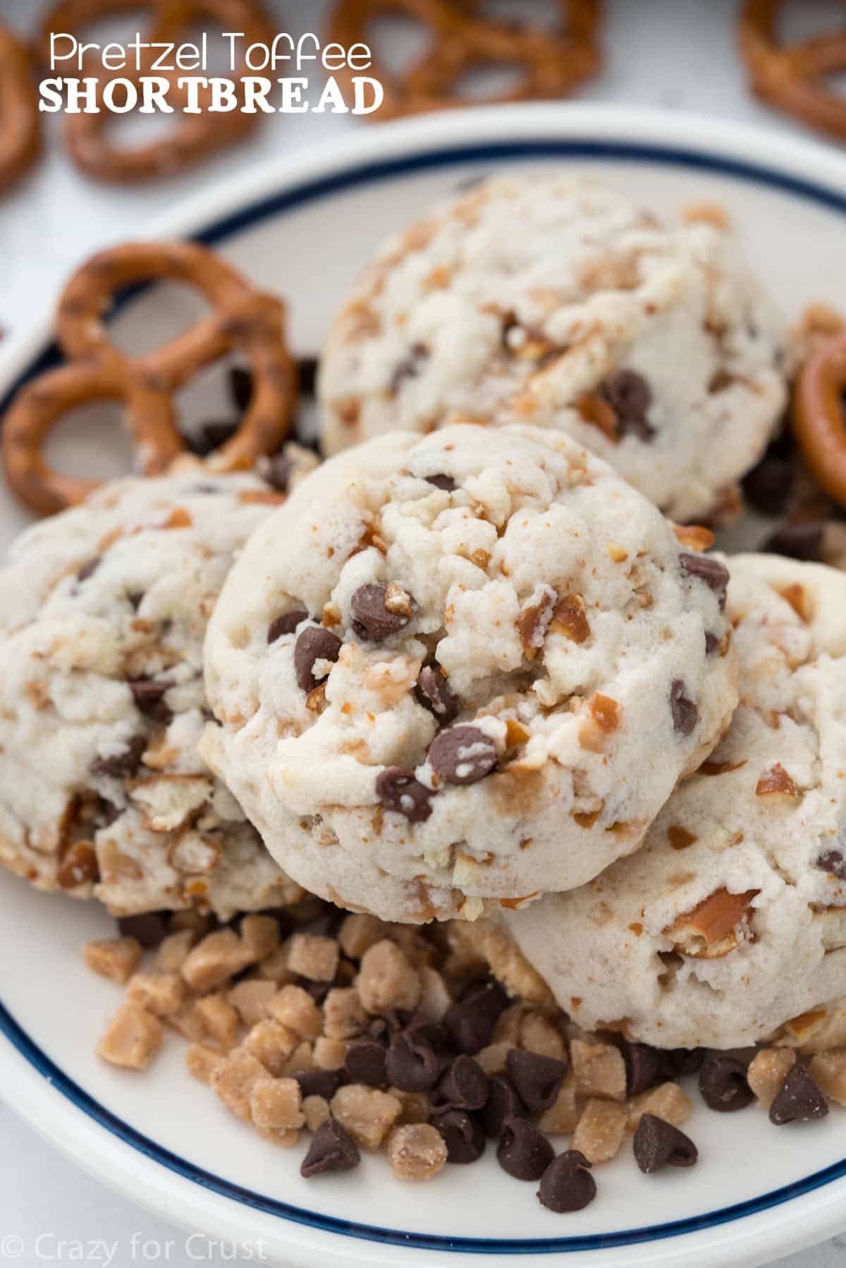 Pretzel Toffee Shortbread on a serving plate surrounded by pretzels, chocolate chips and toffee. 
