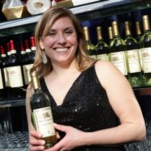 girl smiling in black dress while standing and holding a bottle of white wine