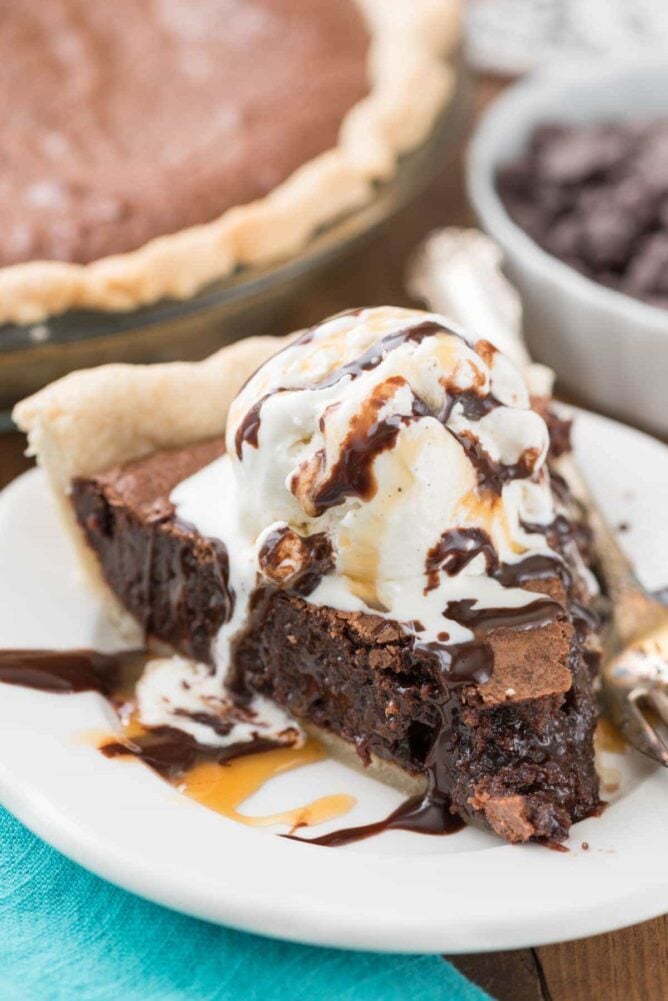 Slice of brownie pie on plate topped with ice cream and hot fudge