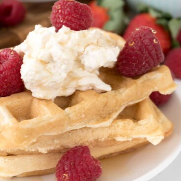Stack of cheesecake waffles with whipped cream and raspberries