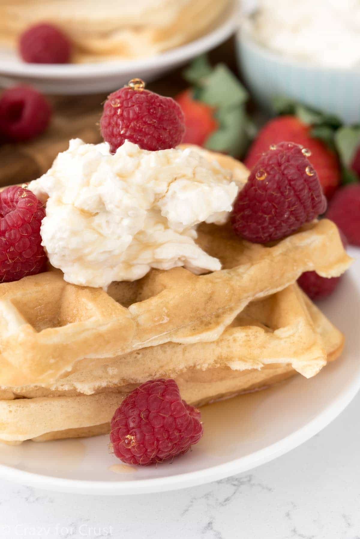 Cheesecake Waffles with raspberries on top on a white serving plate. 