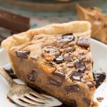 Slice of peanut butter candy bar pie on white plate with silver fork