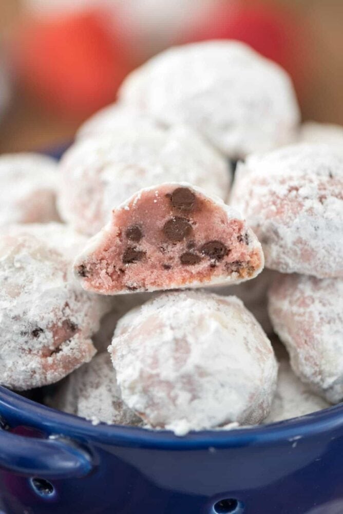 Strawberry chocolate chip snowball cookies in a blue bowl and split in half to show inside of cookie