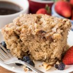 Slice of slow cooker coffee cake on white plate with strawberries and blueberries