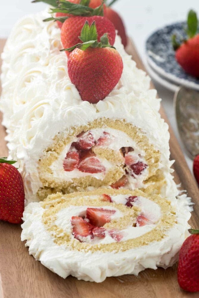 vanilla cake roll filled with strawberries and whipped cream frosting on cutting board