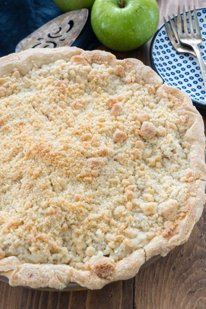 Apple Crumble Pie on a table with a blue and white plate with forks, an apple and a spatula