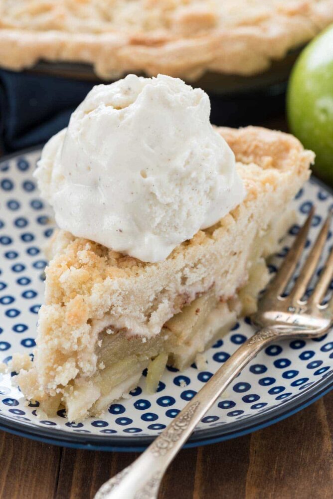 Slice of Apple pie with ice cream sitting on a blue and white plate with a fork