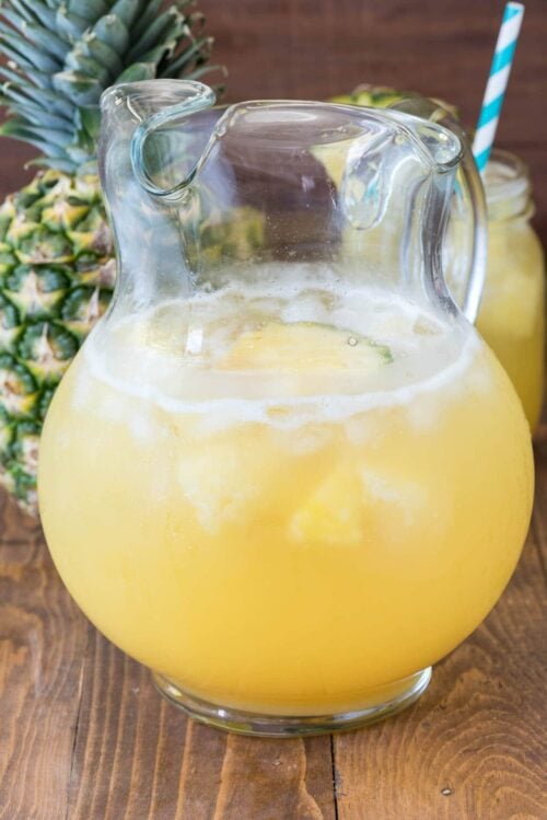 Pineapple punch in a pitcher with a pineapple behind it 