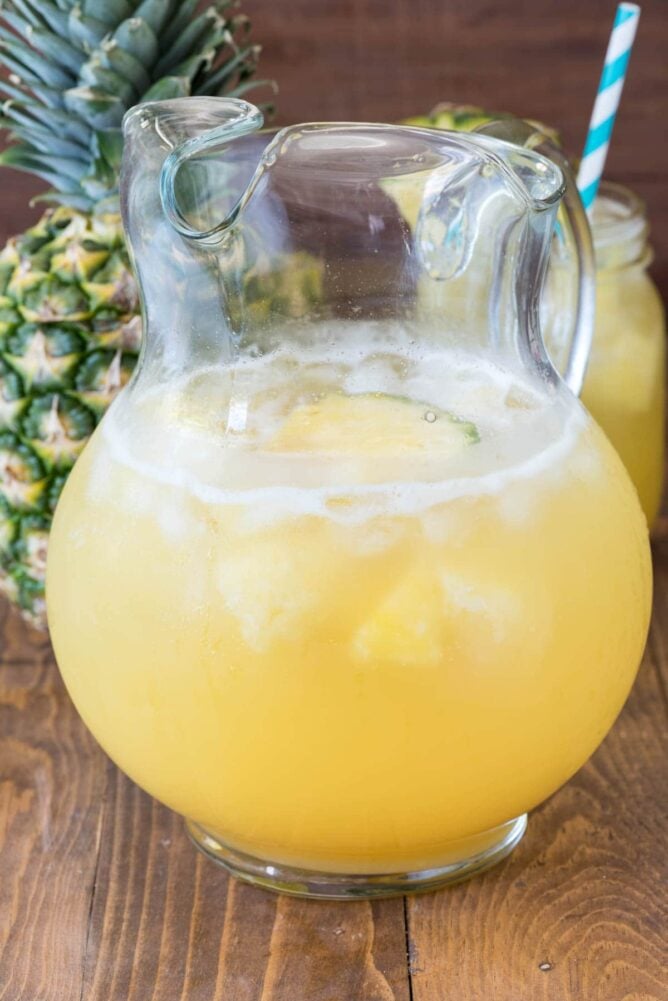 Pineapple Punch in a glass Pitcher with a Pineapple behind