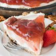 Slice of strawberry pretzel salad pie on white plate with full pie in the background