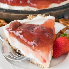 Slice of strawberry pretzel salad pie on white plate with full pie in the background