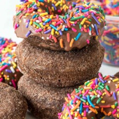 Stack of three perfectly baked chocolate donuts with rainbow sprinkles on top