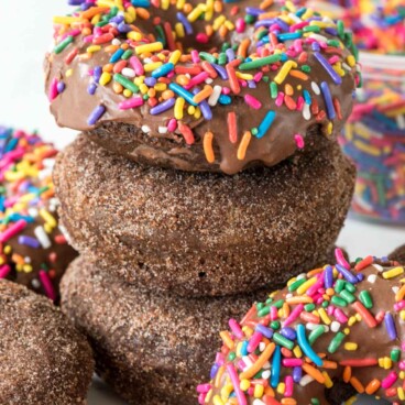 Stack of three perfectly baked chocolate donuts with rainbow sprinkles on top