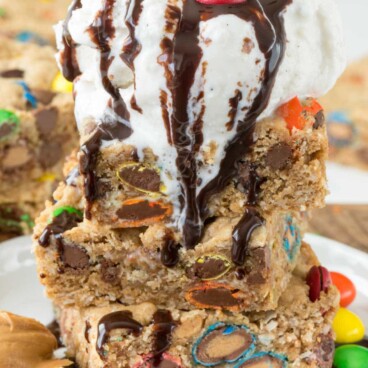 Stack of monster cookie bars with vanilla ice cream scoop on top and chocolate sauce