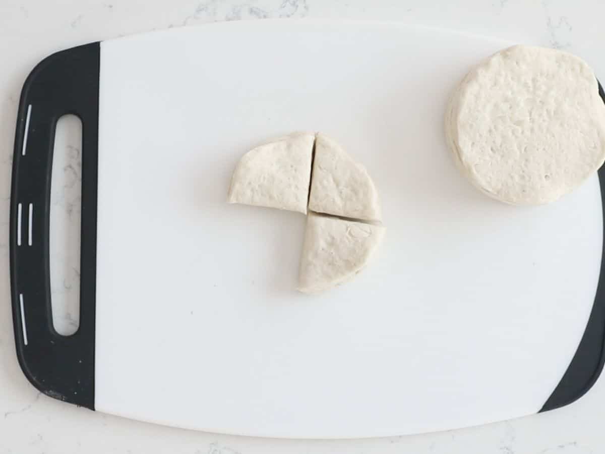 white cutting board with 2 biscuits, one cut in quarters with a piece missing.