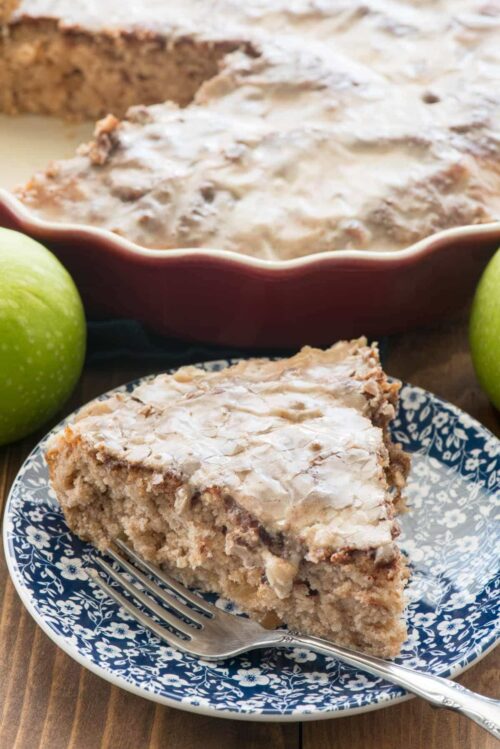 slice of coffee cake on a blue and white plate with a fork. The full coffee cake, less one slice, is behind