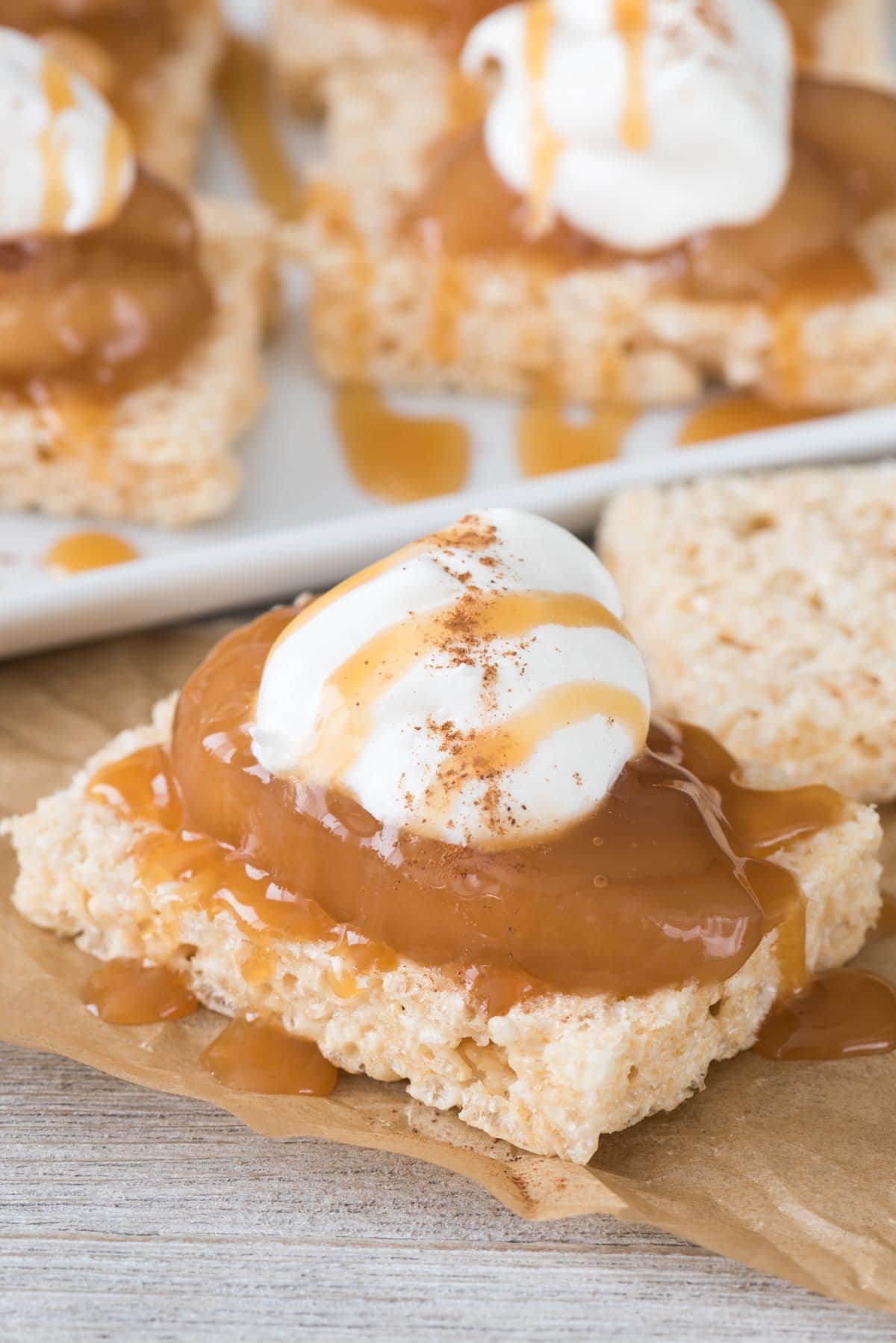 thin rice krispie treat topped with apple pie filling and whipped cream on brown parchment paper