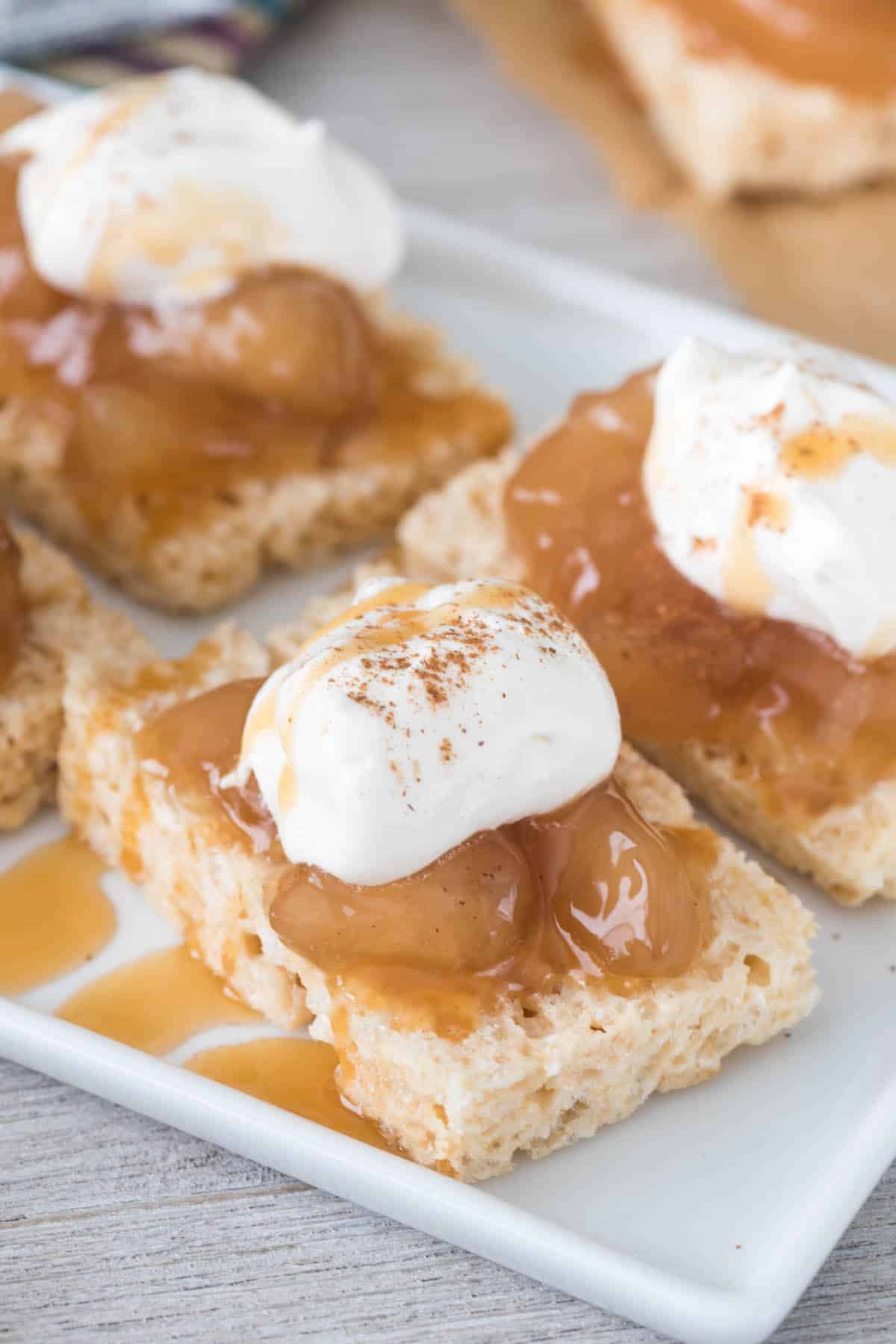 sliced Rice Krispie Treats with apple pie filling and whipped cream on top on white plate