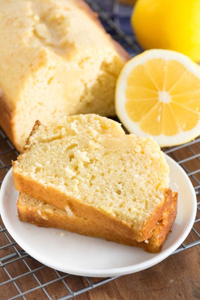 Lemon Quick Bread slices on a white plate with the loaf and lemon slice in the background