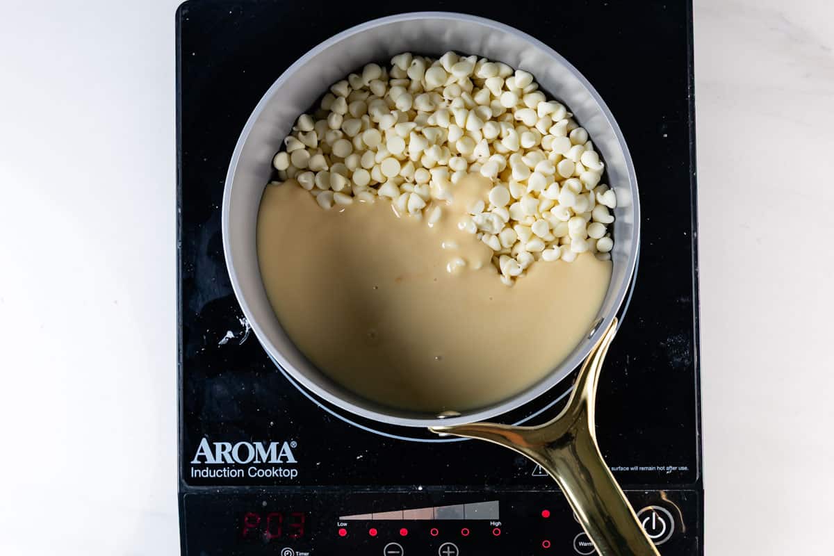 A saucepan with white chocolate chips and sweetened condensed milk sits on an Aroma induction cooktop, ready to be melted and mixed for easy 5 Minute White Chocolate Fudge.