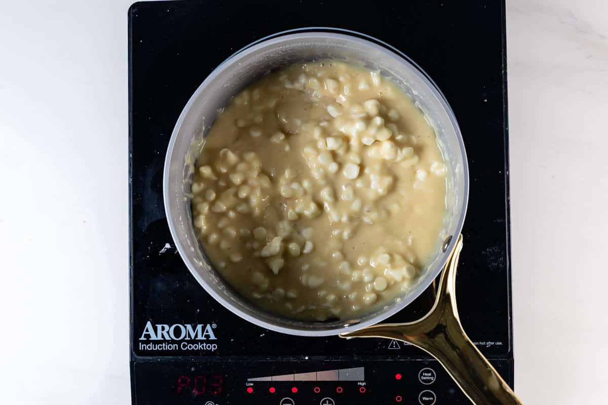 A saucepan filled with creamy corn mixture is placed on an Aroma induction cooktop with a gold handle visible. The thick, chunky mixture of corn kernels in a light yellow sauce looks as irresistible as 5 Minute White Chocolate Fudge.