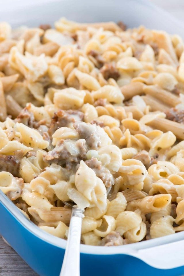 Scooping Sausage Mac & Cheese out of a blue casserole dish. 
