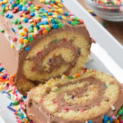 Birthday Cake Roll with one slice cut on a white serving dish