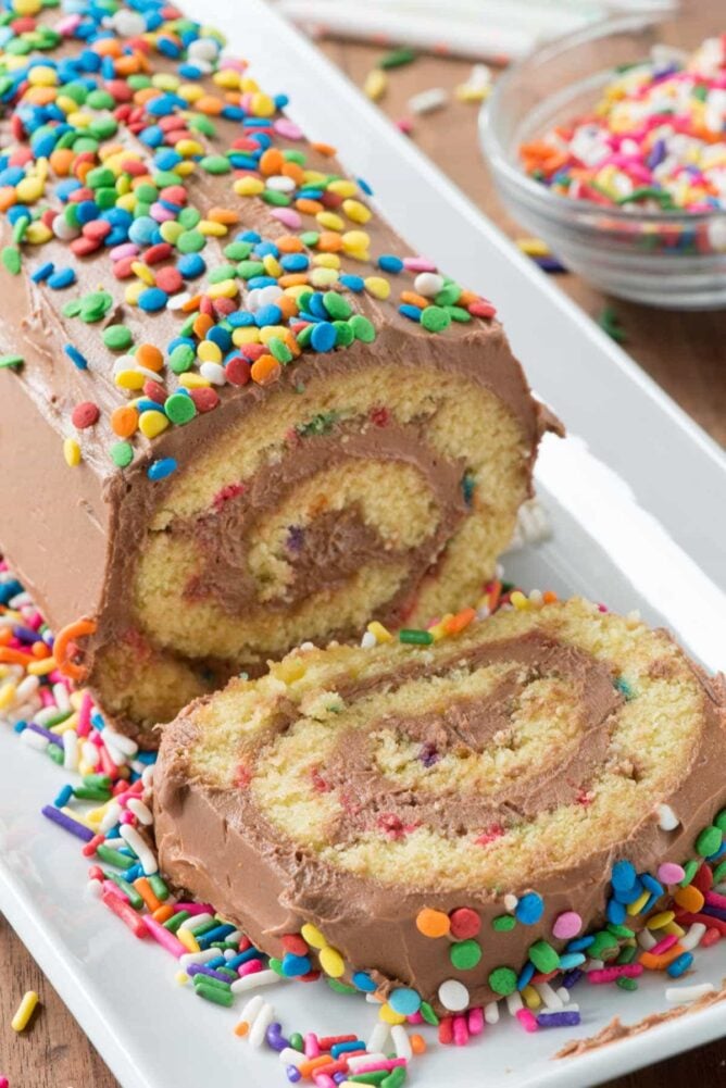 Birthday Cake Roll with one slice cut on a white serving dish