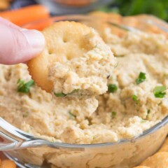 Roasted Garlic Lentil Dip in a glass bowl with a cracker to dip