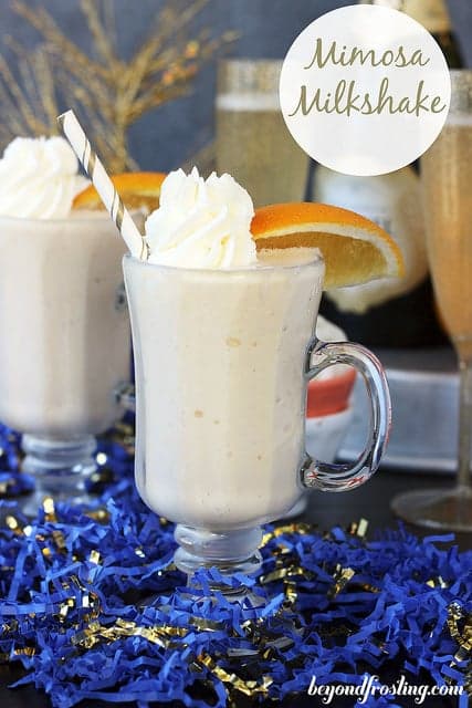 Two Mimosa Milkshakes with straws garnished with whipped cream and sliced oranges. 