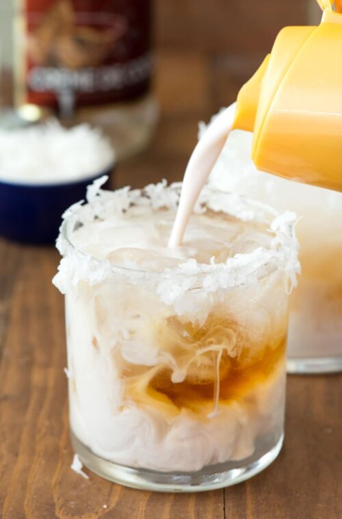 Cocktail in a small glass and cream being poured into the glass