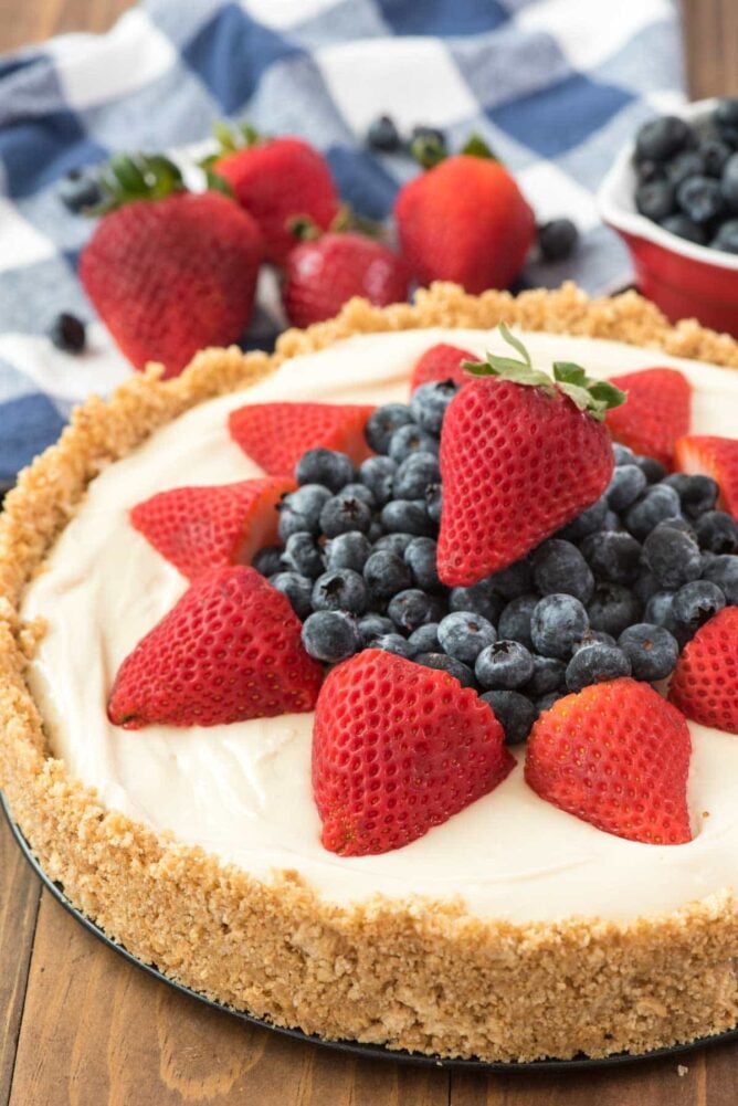 THE BEST NO BAKE CHEESECAKE RECIPE topped with strawberries and blueberries on a wooden board.