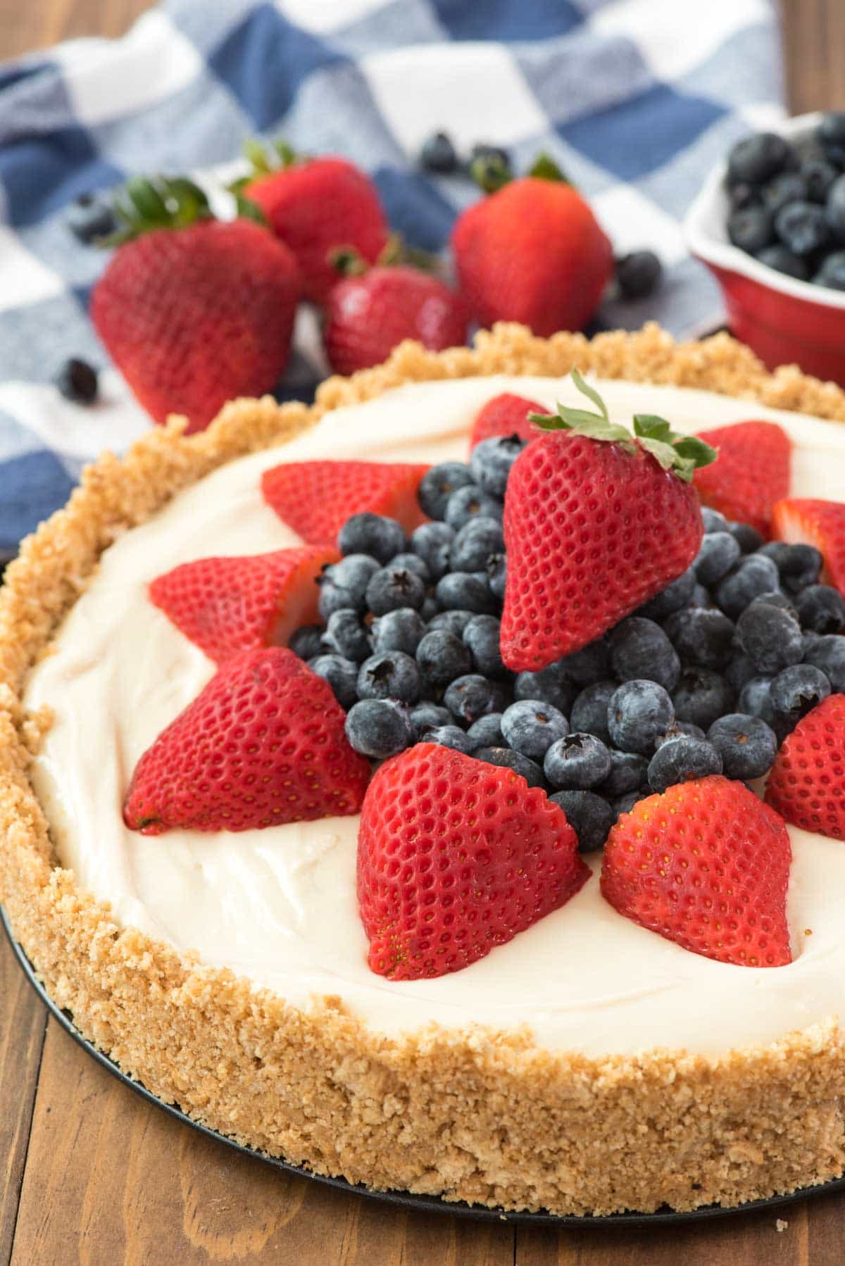 BEST NO BAKE CHEESECAKE RECIPE EVER topped with blueberries and strawberries on a wooden board. 